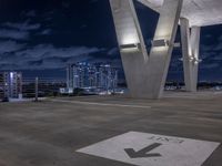 a parking sign pointing to the direction of an exit with buildings in the background and clouds in the sky