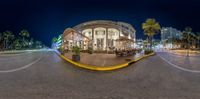 an image of a circular restaurant at night time with traffic coming down the road and a lot of palm trees in front