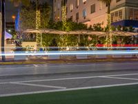 a city intersection at night with lights in the background and palm trees on a sidewalk