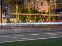 a city intersection at night with lights in the background and palm trees on a sidewalk