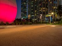 empty city street in front of brightly colored building at night time on beachfront with large pink ball