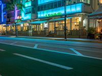 a street at night with palm trees and lights on the building and on the side of the road