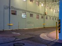 a street corner at night with lights on and green building in the background - -