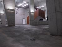 a parking lot with concrete pillars and ceiling lights in a warehouse building with orange doors