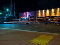 the side walk of an intersection at night with traffic lights in the background and a red light