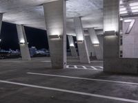 a concrete area with columns and white markings on it at night time with lights above