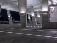 a concrete area with columns and white markings on it at night time with lights above