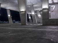 a concrete area with columns and white markings on it at night time with lights above