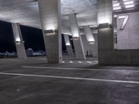 a concrete area with columns and white markings on it at night time with lights above