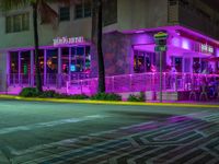 a cafe with neon lights, near the street with people sitting outside at night, and in front of a multi - colored building