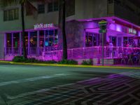 a cafe with neon lights, near the street with people sitting outside at night, and in front of a multi - colored building