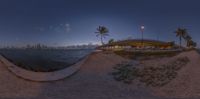 an elevated walkway stretches into the ocean at twilight by a beach with palm trees and buildings