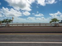 an empty highway in the city with an ocean in the background and blue skies with fluffy clouds