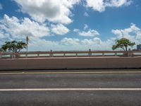 an empty highway in the city with an ocean in the background and blue skies with fluffy clouds