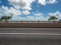 an empty highway in the city with an ocean in the background and blue skies with fluffy clouds