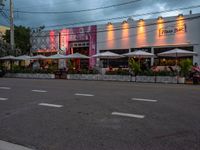 an outside restaurant has white tables and chairs and several umbrellas at the entrance of the building