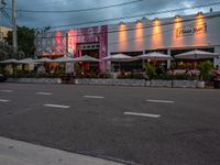 an outside restaurant has white tables and chairs and several umbrellas at the entrance of the building