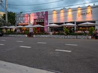 an outside restaurant has white tables and chairs and several umbrellas at the entrance of the building