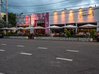 an outside restaurant has white tables and chairs and several umbrellas at the entrance of the building