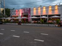 an outside restaurant has white tables and chairs and several umbrellas at the entrance of the building