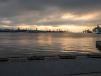 a body of water with a large ship in the background in a bay during sunset