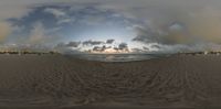 the view from a panoramic angle shows the sand and water at the beach with a beach umbrellas in the foreground