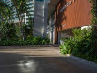 the entrance to an apartment with palms trees and bushes in the foreground, next to a concrete driveway