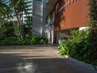 the entrance to an apartment with palms trees and bushes in the foreground, next to a concrete driveway