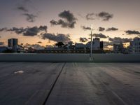 the large open concrete parking lot is in the foreground as the sun sets over the city