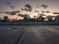 the large open concrete parking lot is in the foreground as the sun sets over the city