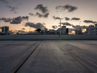 the large open concrete parking lot is in the foreground as the sun sets over the city