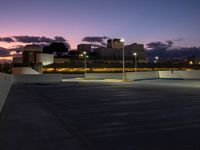 a parking lot at night with two lights on and a long row of building along the street