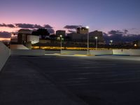 a parking lot at night with two lights on and a long row of building along the street