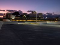 a parking lot at night with two lights on and a long row of building along the street