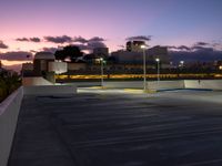 a parking lot at night with two lights on and a long row of building along the street