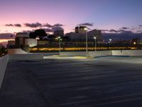 a parking lot at night with two lights on and a long row of building along the street