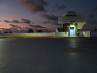 parking garage with no sign at sunset time with clouds in the sky behind it and parking lights in the distance