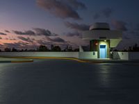 parking garage with no sign at sunset time with clouds in the sky behind it and parking lights in the distance