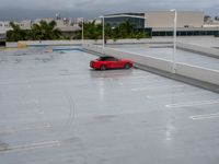 a red sports car in an empty parking lot area next to buildings in the background