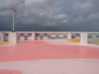 an empty parking lot next to the ocean, with a red floor and pink and yellow painted floors