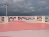 an empty parking lot next to the ocean, with a red floor and pink and yellow painted floors