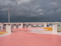 an empty parking lot next to the ocean, with a red floor and pink and yellow painted floors