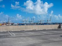 some parking spaces near a fence with cranes in the distance and one of them standing with its arms in the air