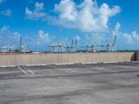 some parking spaces near a fence with cranes in the distance and one of them standing with its arms in the air