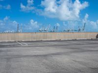 some parking spaces near a fence with cranes in the distance and one of them standing with its arms in the air