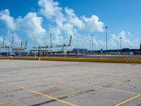 an empty parking lot filled with lots of buildings and trucks in the background of a cloudy blue sky