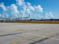 an empty parking lot filled with lots of buildings and trucks in the background of a cloudy blue sky