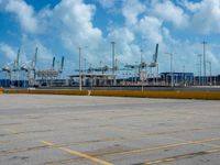 an empty parking lot filled with lots of buildings and trucks in the background of a cloudy blue sky