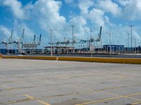 an empty parking lot filled with lots of buildings and trucks in the background of a cloudy blue sky