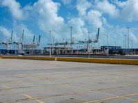 an empty parking lot filled with lots of buildings and trucks in the background of a cloudy blue sky